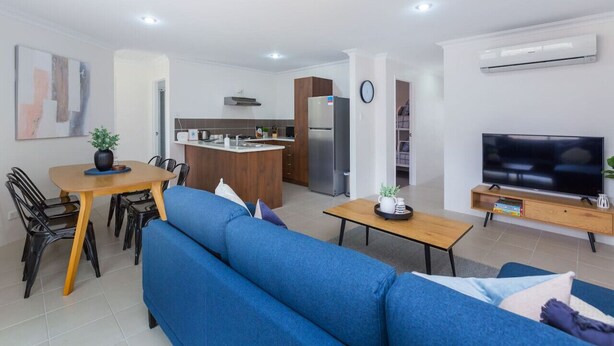 Una sala de estar moderna con un sofá azul, una mesa de centro de madera y un televisor sobre un mueble de madera.
