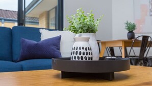 Una sala moderna con un sofá azul, un florero blanco con plantas verdes y una mesa de centro de madera.