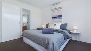 Un dormitorio moderno con una cama grande, una mesita de noche con lámpara y aire acondicionado instalado en la pared.