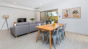 Una sala de estar moderna con un sofá gris, una mesa de comedor de madera con sillas, un televisor y obras de arte en la pared.
