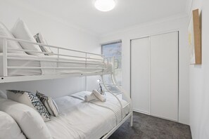 A bunk bed with a desk and chair, a bedside lamp, and a wardrobe in a room with white walls.