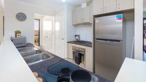 A modern kitchen with a stainless steel refrigerator, a built-in oven, and a gas stove. There is a sink with a double basin and a clock on the wall. - Family perfection in quiet & convenient location! (Balcatta)