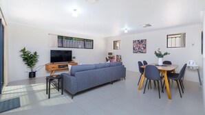 A modern living room with a grey sofa, a TV, a dining table with chairs, and a small side table. - Family perfection in quiet & convenient location! (Balcatta)