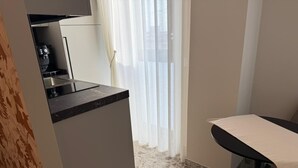 Une cuisine compacte avec un plan de travail et un évier, une table à manger avec une chaise, et une fenêtre avec des rideaux légers.