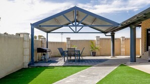 Un patio couvert avec une table et des chaises, une pelouse artificielle et un mur en briques.