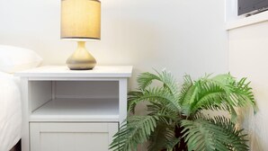 Una mesita de noche blanca con una lámpara y una planta de helecho.