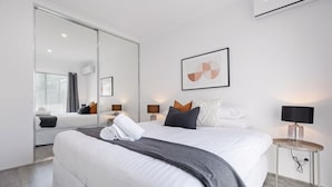 Ein modernes Hotelzimmer mit einem großen Bett, einem Nachttisch mit Lampe, einer Wand-Klimaanlage und einem großen Spiegel.