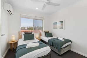 A bedroom with two beds, a window, a ceiling fan, and a wall-mounted air conditioner. - Seaside townhouse escape... stroll to the sea! (Scarborough)
