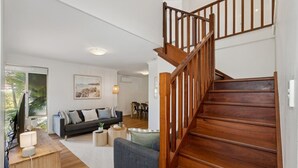 A modern living room with a wooden staircase, a sofa, a coffee table, and a dining area. - Seaside townhouse escape... stroll to the sea! (Scarborough)