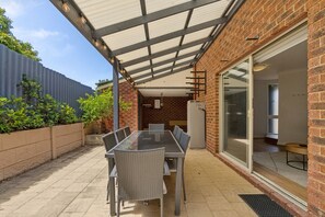A covered patio with a table and chairs, a brick wall, and a sliding glass door leading to an interior space. - Seaside townhouse escape... stroll to the sea! (Scarborough)