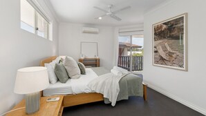 A bedroom with a bed, bedside table, lamp, air conditioning unit, and a balcony with chairs. - Seaside townhouse escape... stroll to the sea! (Scarborough)