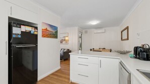 A modern kitchen with white cabinetry, a black refrigerator, a dining area with a wooden table, and a view of the outdoors. - Seaside townhouse escape... stroll to the sea! (Scarborough)