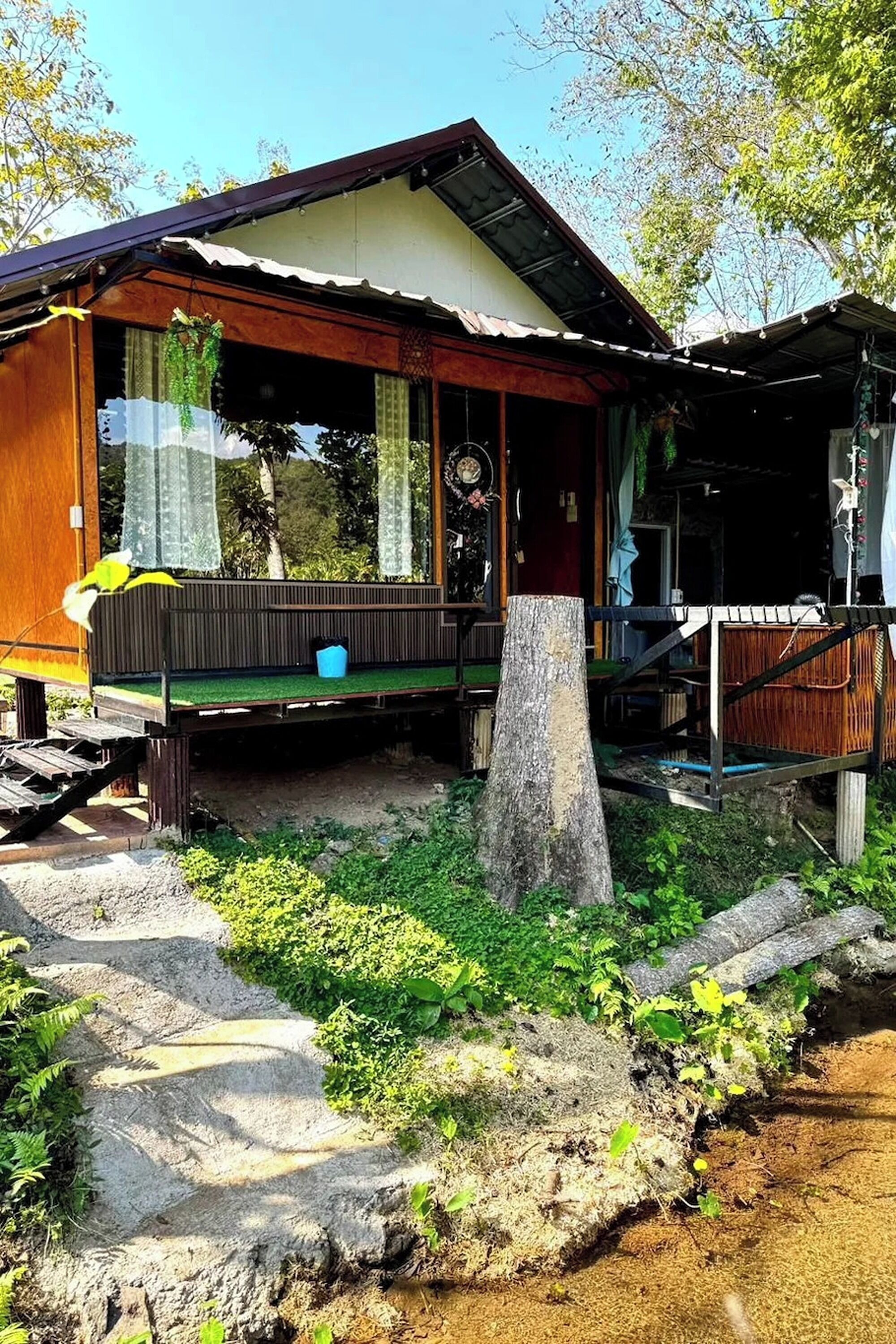A wooden house with a porch, a small deck, and a tree stump in front.