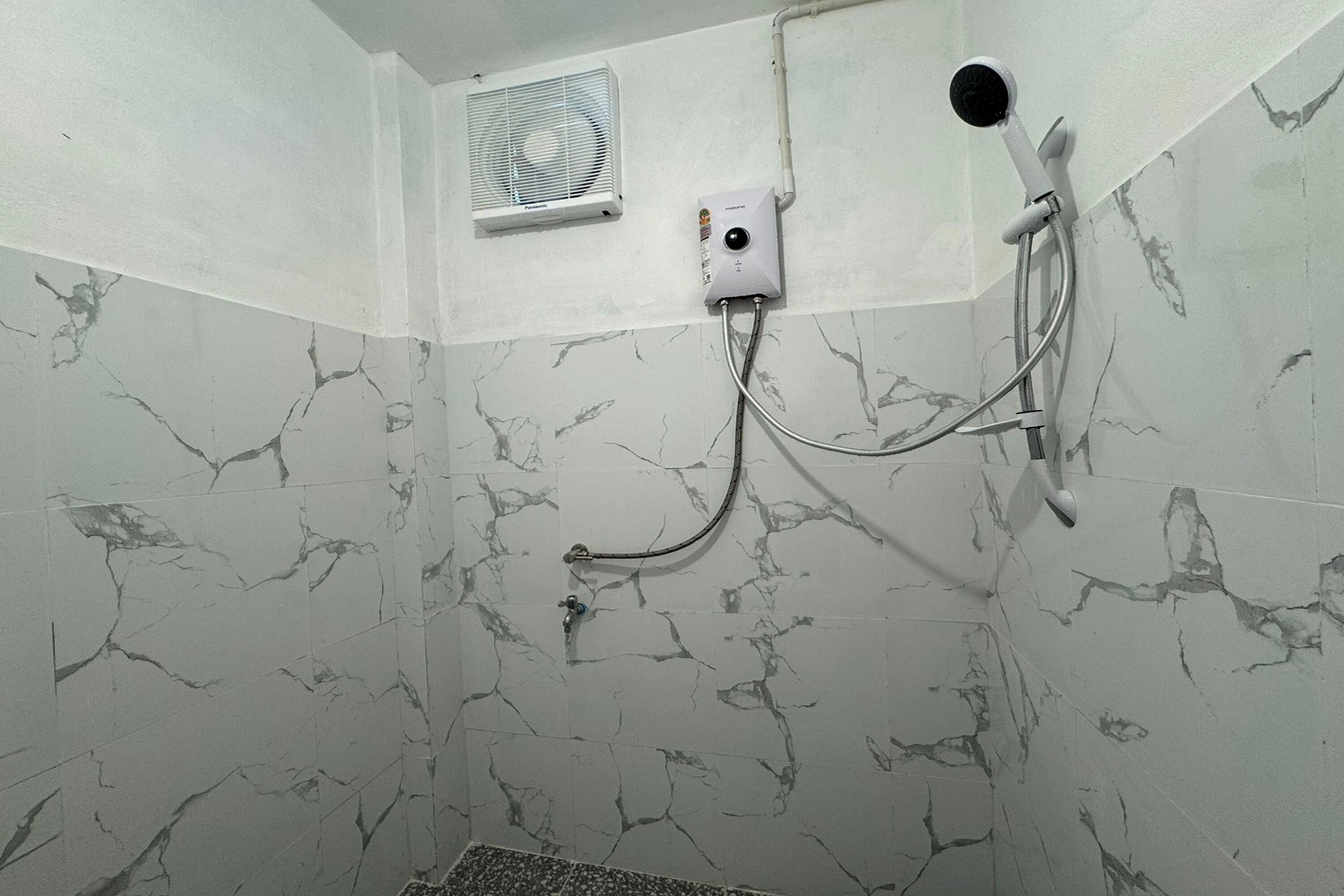 A bathroom with a shower, a handheld showerhead, a handheld shower attachment, and a wall-mounted fan.