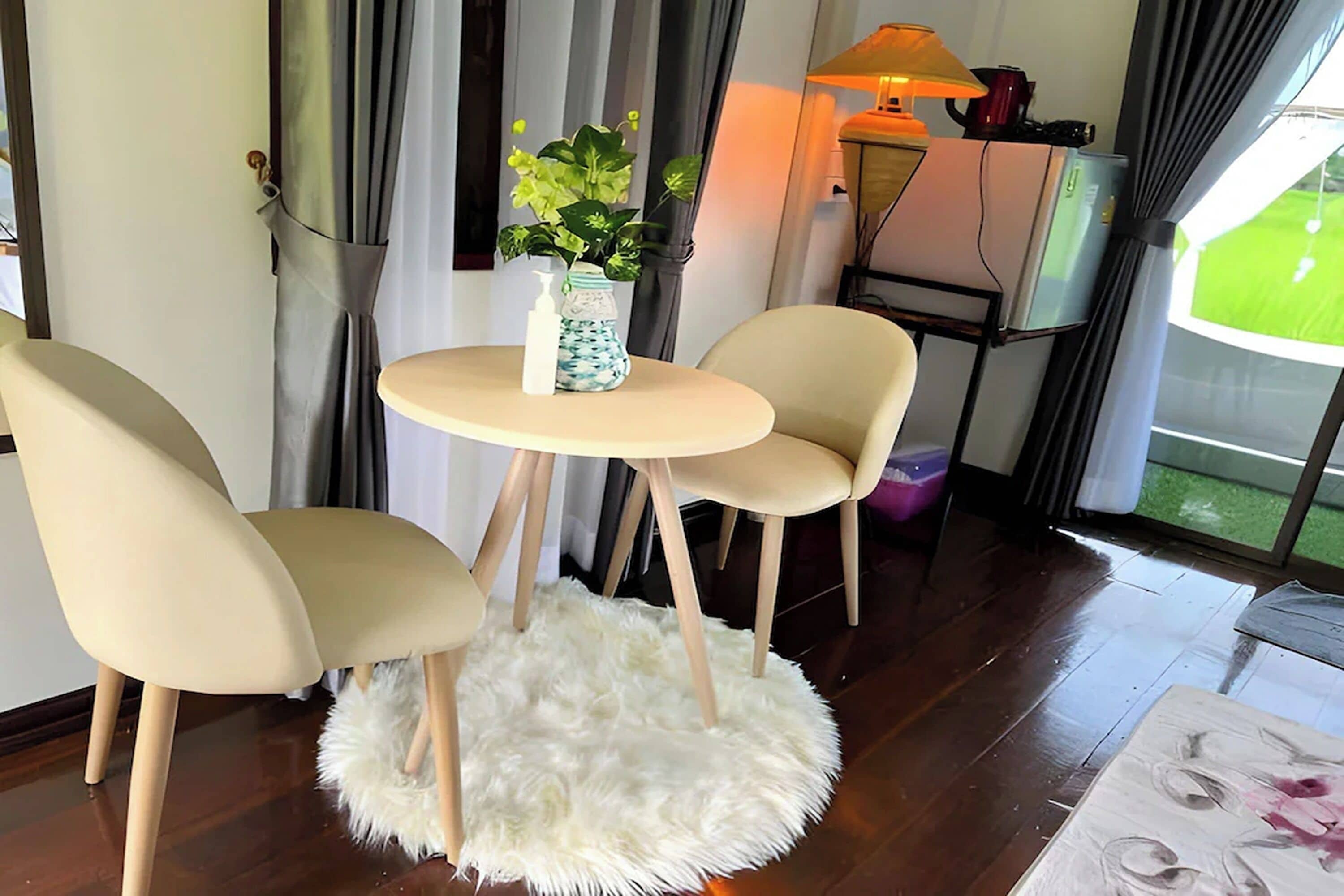 Une pièce avec une table ronde, deux chaises, un tapis blanc et moelleux, une plante et une lampe.