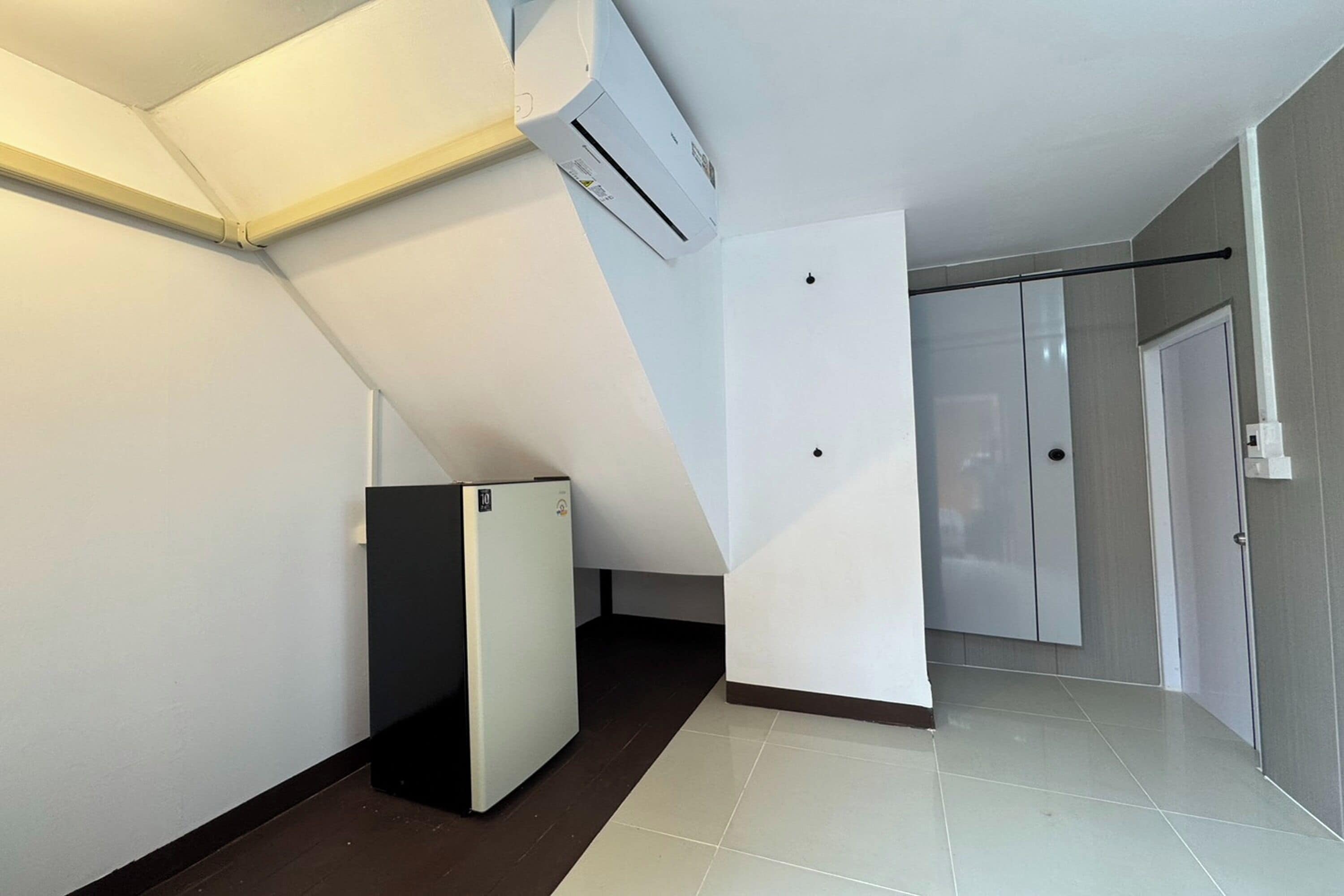 Una habitación con piso de baldosas blancas, un refrigerador negro, una puerta blanca y una pared blanca con una ventana.