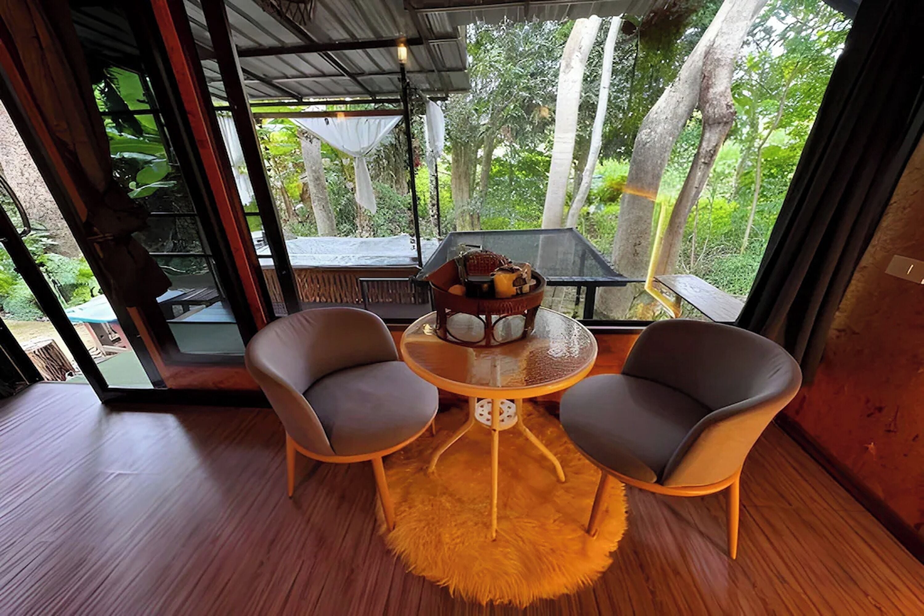 A room with a glass door leading to a deck, two chairs around a small table with a bowl of fruit, and a wooden floor.