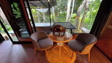 A room with a glass door leading to a deck, two chairs around a small table with a bowl of fruit, and a wooden floor.