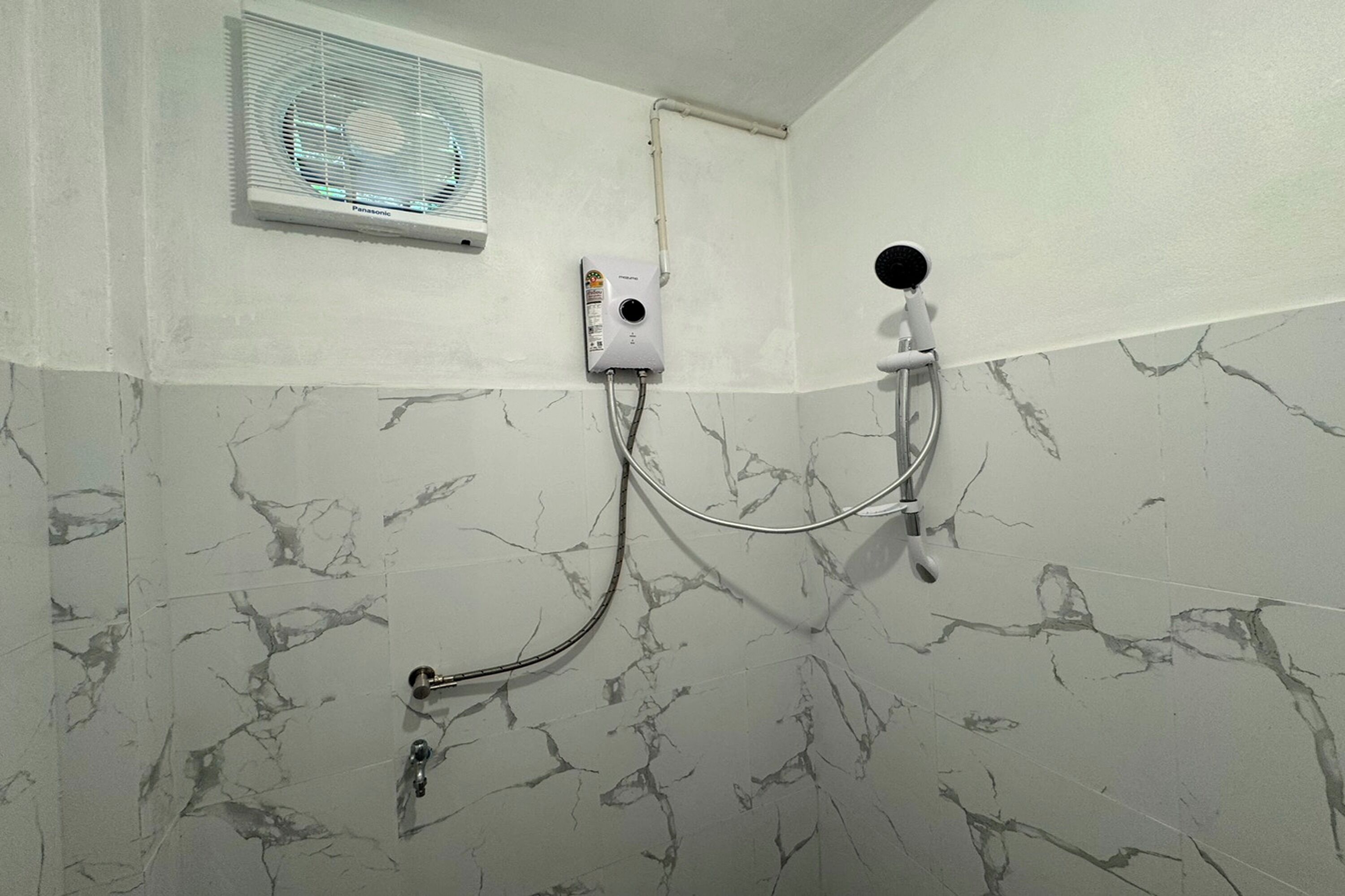 A bathroom with a shower, a wall-mounted fan, and a marble-patterned wall.
