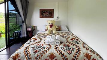Ein Schlafzimmer mit einem großen Bett, einem Teddybären, einem Bild und Blick auf Grünfläche draußen.