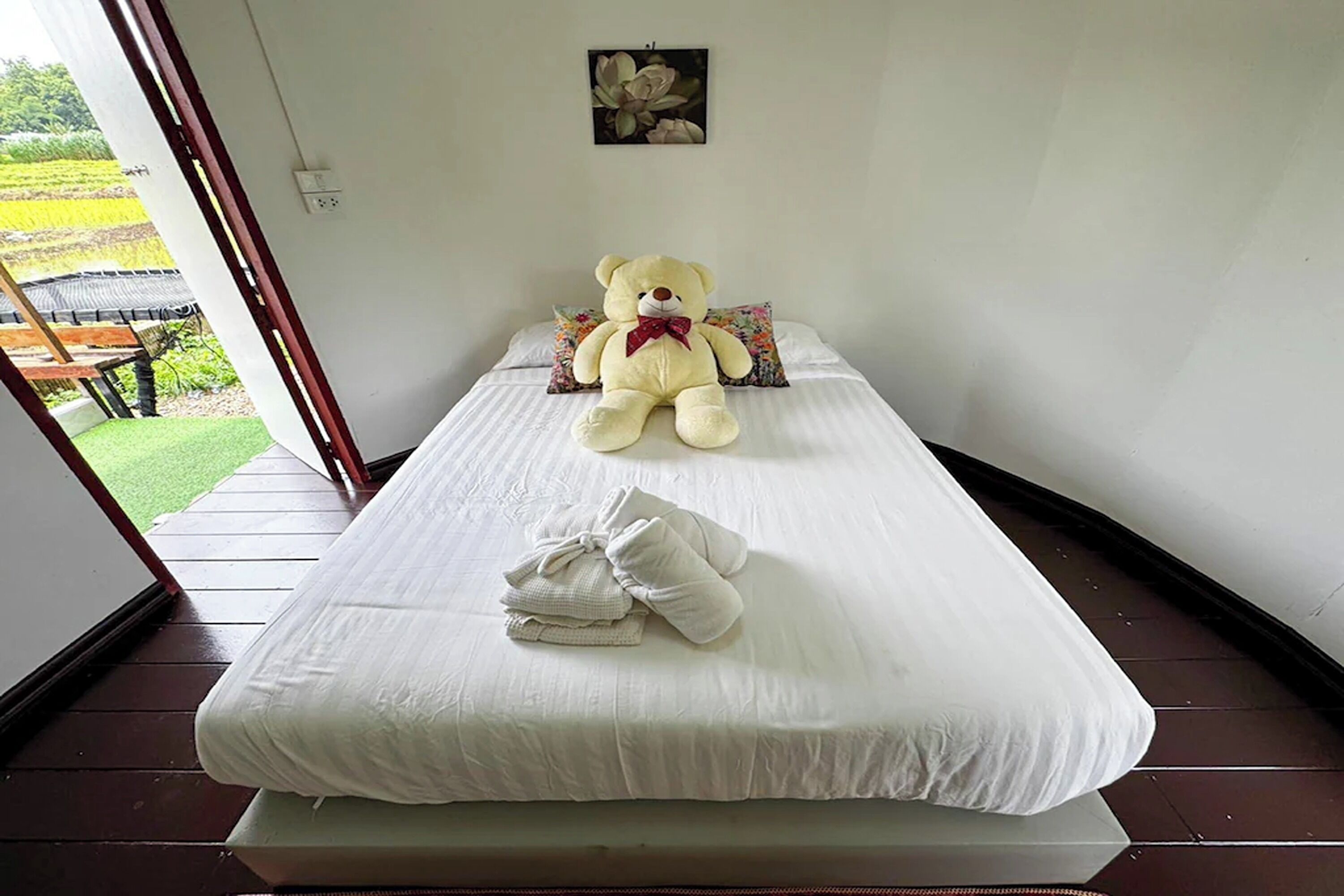 A single bed with a white mattress, a large teddy bear, and a folded towel on the bed.