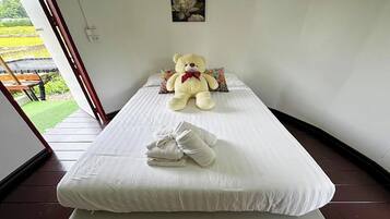 A single bed with a white mattress, a large teddy bear, and a folded towel on the bed.