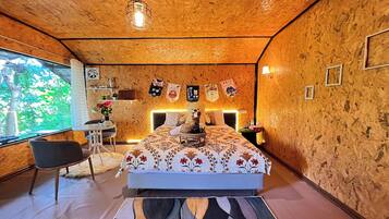 A bedroom with a bed, a desk, and a chair. There is a window on the left side.