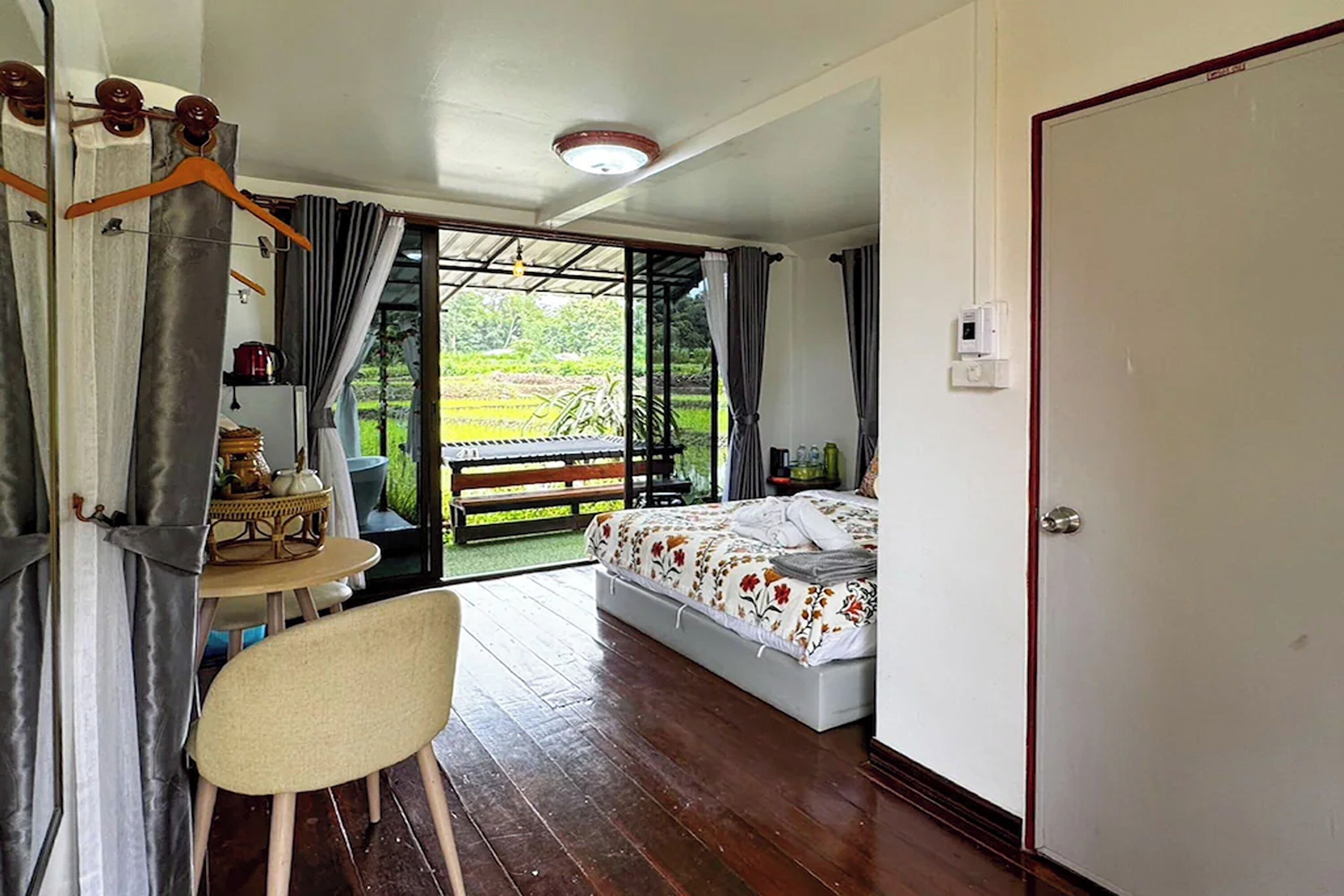 A bedroom with a bed, a desk with a chair, a wardrobe, and a view of a garden through an open door.