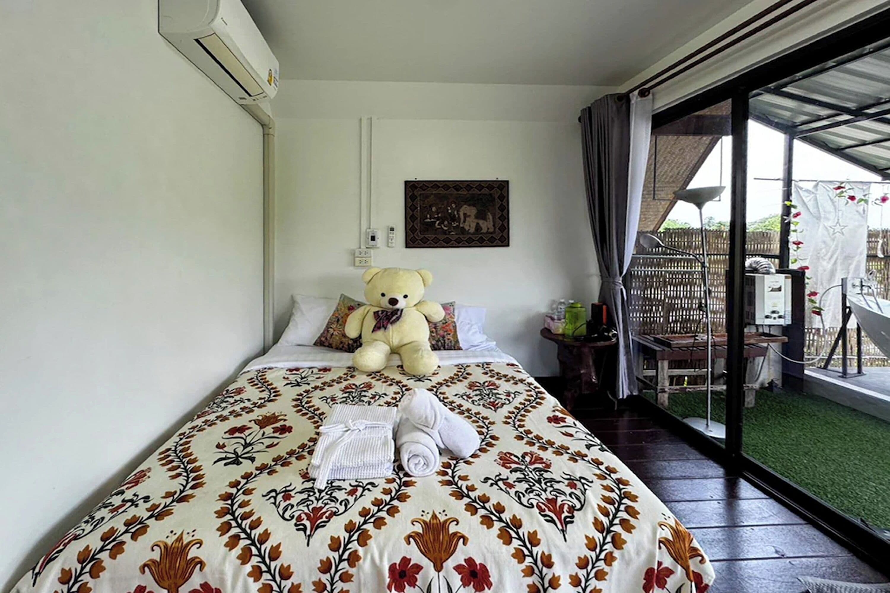 A bedroom with a bed, a teddy bear, a painting, and a view of the outdoors.