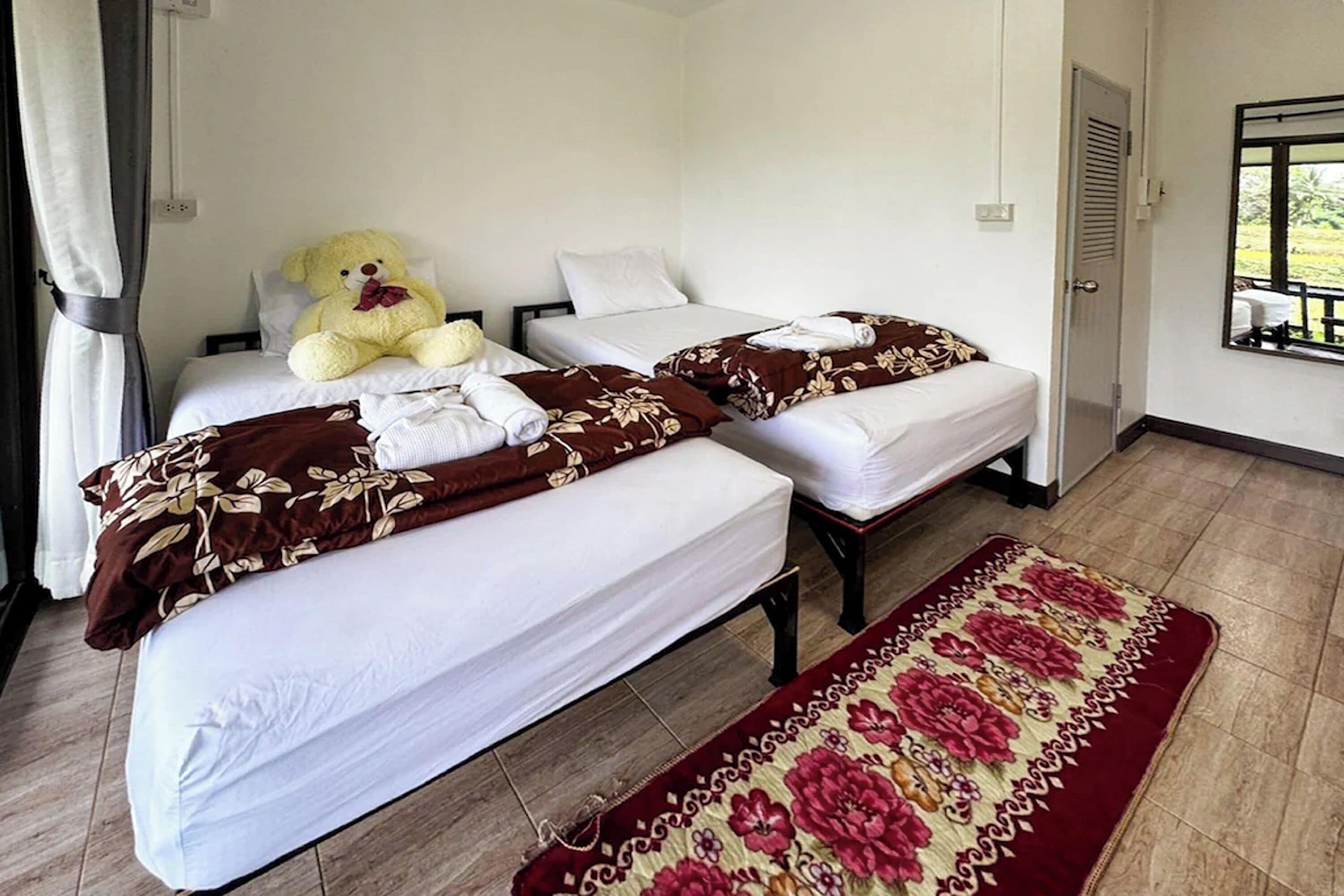 Habitación de hotel con dos camas, un peluche grande sobre una de ellas y un tapete floral en el suelo.