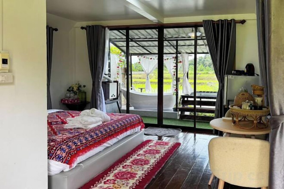 Un dormitorio con cama, una mesita y vista a un jardín por una puerta corredera.