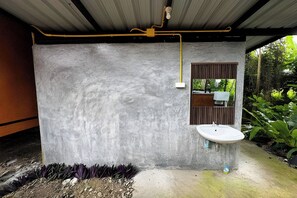 Une salle de bain avec un mur en béton, une fenêtre avec un volet en bois et un lavabo blanc.