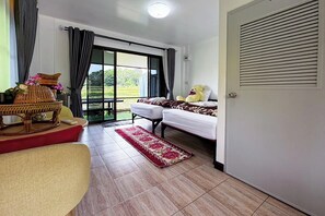 A hotel room with a bed, a sofa, a dining table with a basket and flowers, a window with curtains, and a view of greenery outside. - Nansilarom Boutique Resort (Pua)