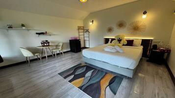 Un dormitorio moderno con una cama grande, un escritorio y una silla. Hay apliques decorativos y un estante pequeño con objetos encima.