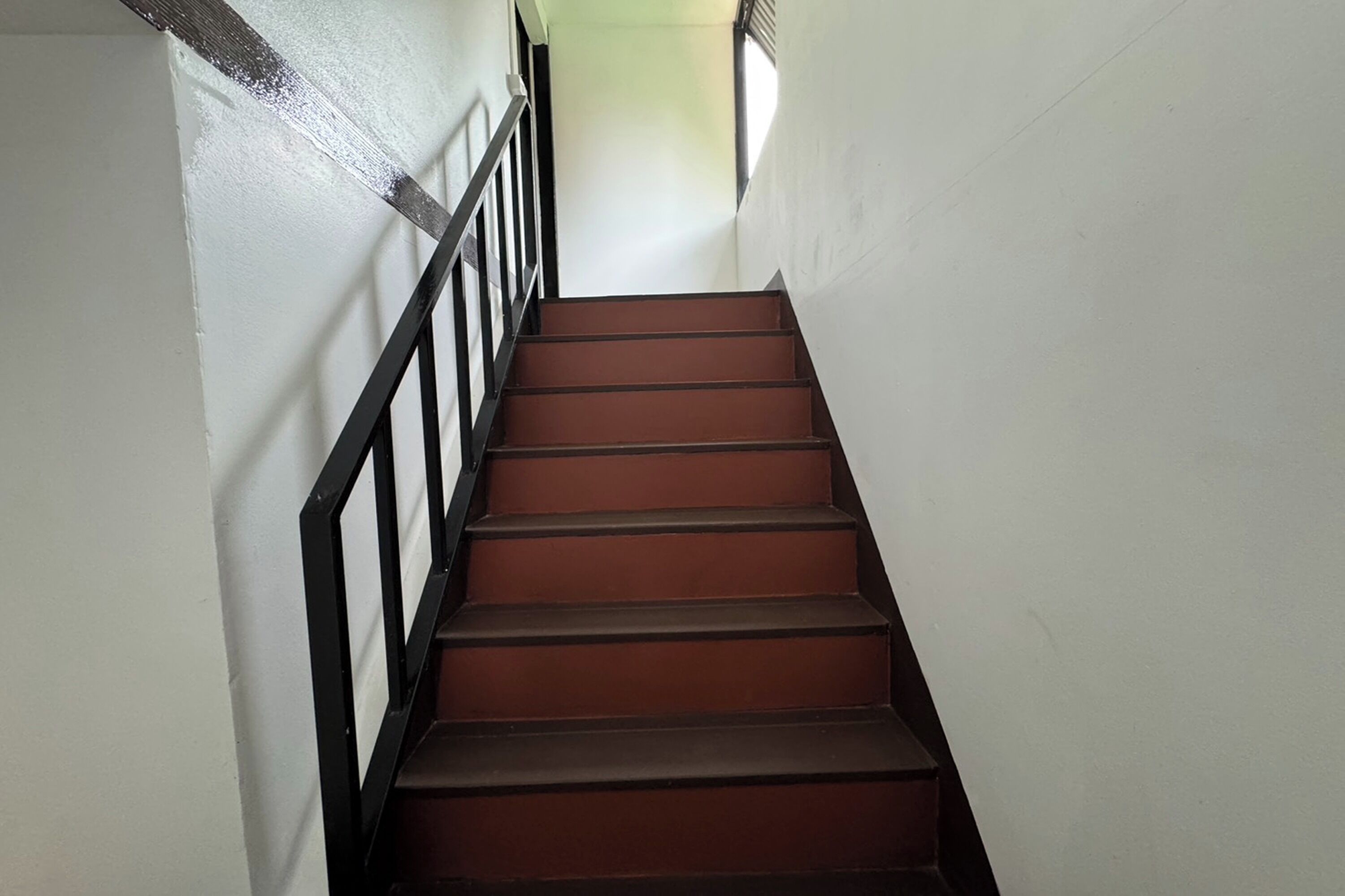 Una escalera con barandilla negra y escalones marrones.