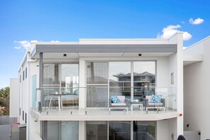 En moderne bygning med to etager, store glasvinduer og en balkon med siddepladser.