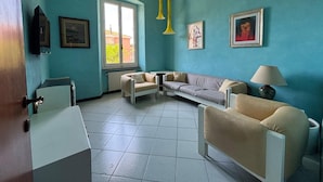 A room with teal walls, a sofa, a chair, a lamp, and a window with a view of greenery. - Apartment in Chiavari (Chiavari)
