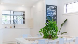 Un espace repas moderne avec une table et des chaises blanches, une plante en pot et un mur orné d’une affiche représentant un nuage de mots.