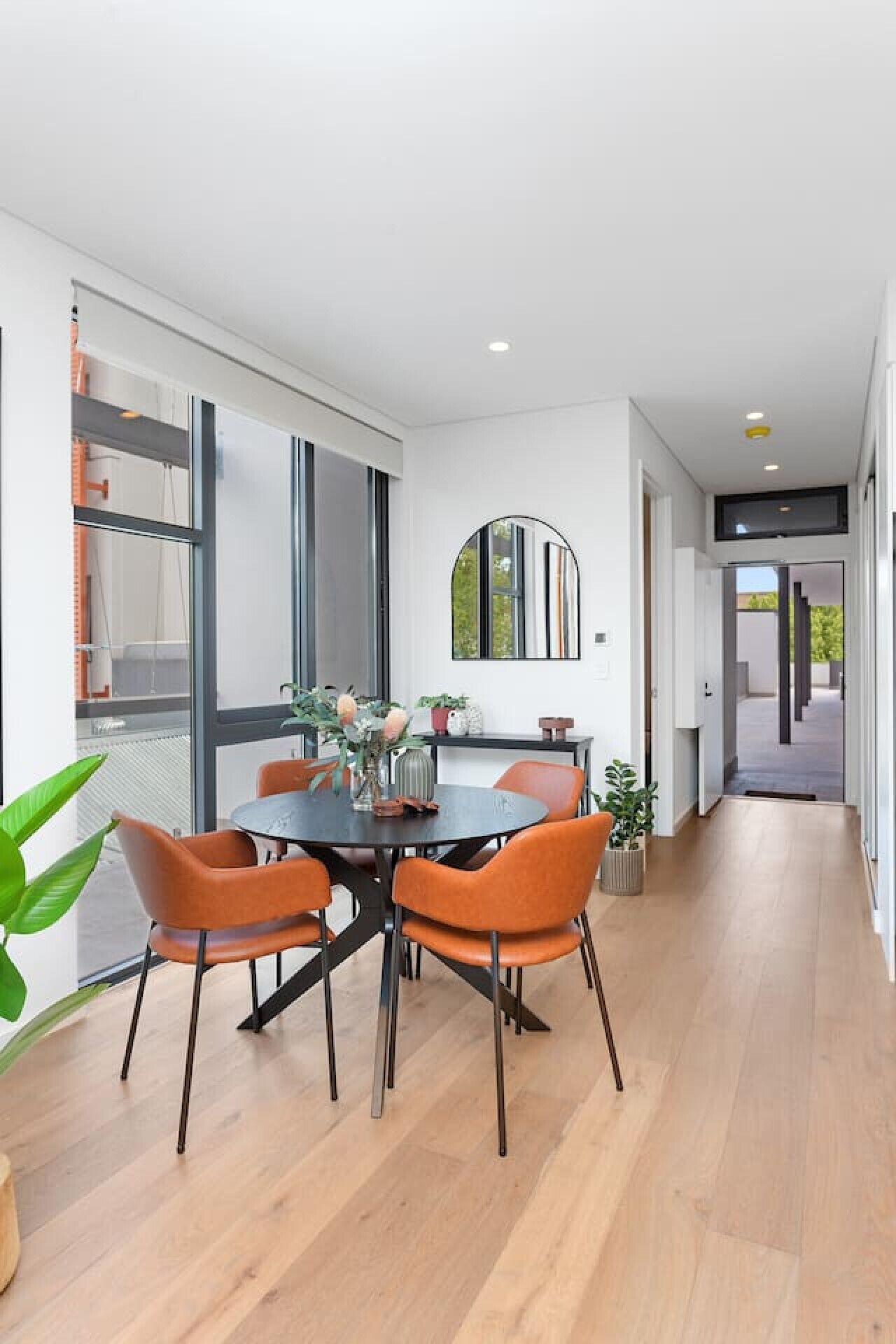 A modern dining area with a round table and orange chairs, large windows, and a minimalist design.