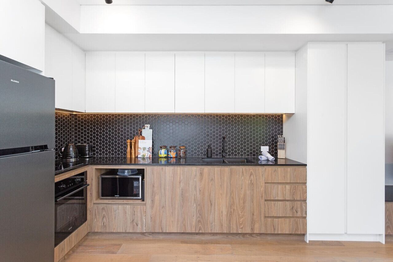 A modern kitchen with white cabinets, a black countertop, and a hexagonal tile backsplash.