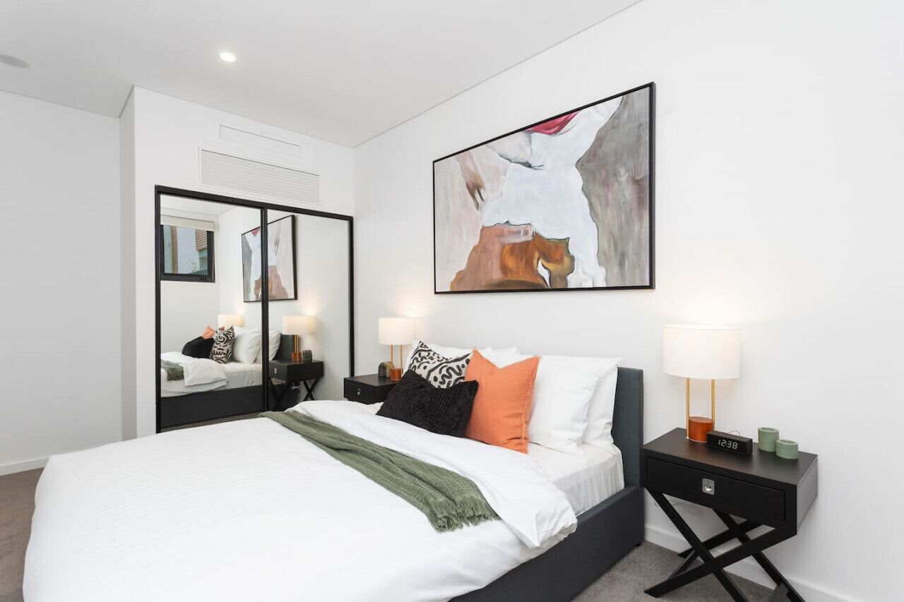A modern bedroom with a large bed, bedside tables, a mirror, and a painting.