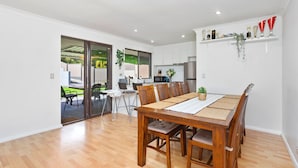 A spacious dining area with a wooden table and chairs, a kitchen in the background, and a sliding glass door leading to an outdoor patio. - Incredible family home in the heart of Beldon! (Beldon)