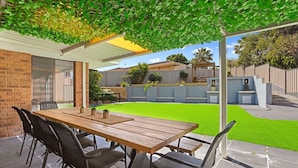 An outdoor patio with a wooden table and chairs, a covered area with a pergola, and a well-maintained lawn. - Incredible family home in the heart of Beldon! (Beldon)