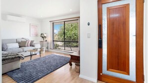A modern living room with a sofa, a coffee table, and a rug. There is a wooden door with a glass panel and a window with blinds. - Incredible family home in the heart of Beldon! (Beldon)