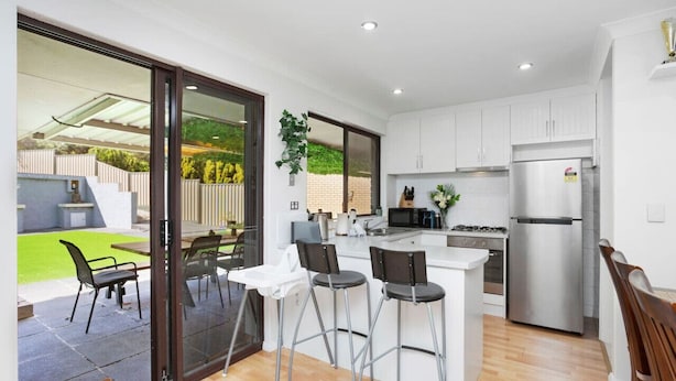 A modern kitchen with a central island, stainless steel appliances, and a sliding glass door leading to a patio area. - Incredible family home in the heart of Beldon! (Beldon)