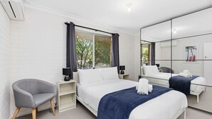 A hotel room with a large bed, a chair, a nightstand, a mirror, and a window with curtains.