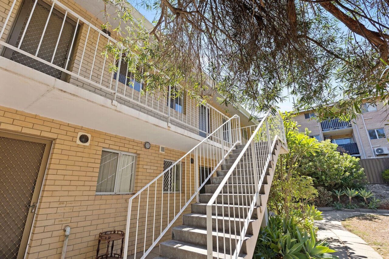 Un edificio de varios pisos con una escalera central, asientos exteriores y un jardín ajardinado.