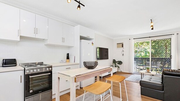 A modern kitchen with white cabinets, a stainless steel stove, and a dining area with stools.