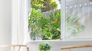 A room with two wooden chairs, a small round table with a potted plant, and a window with a view of greenery outside. - Dreamy getaway awaits for the ultimate relaxation! (Hamersley)