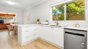 A modern kitchen with white cabinetry, a built-in dishwasher, and a window with a view of greenery. - Dreamy getaway awaits for the ultimate relaxation! (Hamersley)